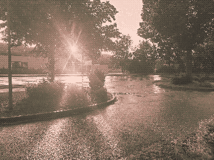 a sepiatone photo of light peering through two trees in a lonely parking lot